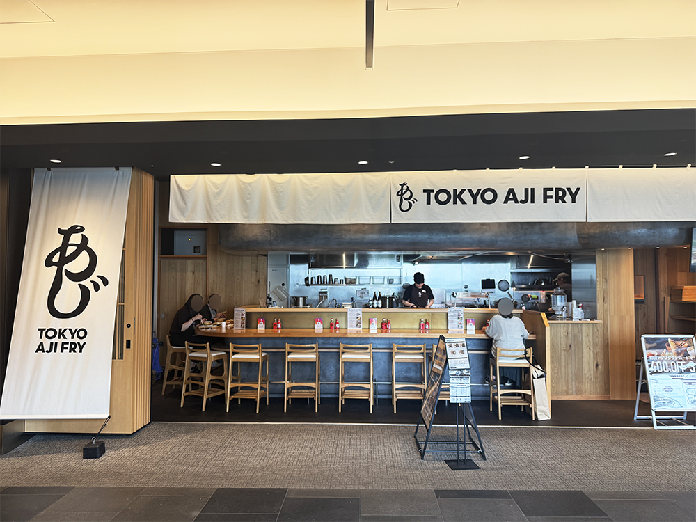 羽田エアポートガーデン2階にある「トーキョーアジフライ」の店舗外観と、木目のカウンター席。