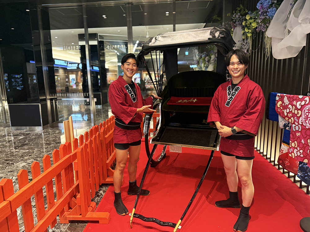 羽田エアポートガーデンの館内に置かれた黒塗りの人力車と、赤い法被を着た2人の俥夫。