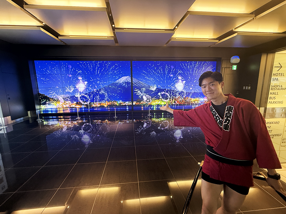 夜景のようにライトアップされた華やかな館内を背景に、人力車の横でポーズを決める俥夫の堤勇真。