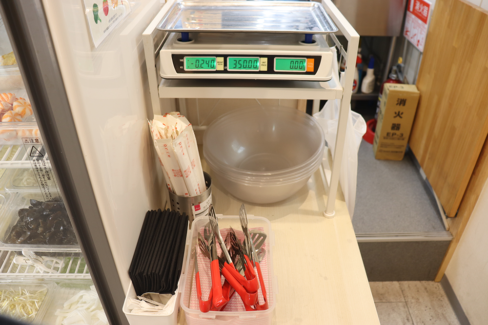 冷蔵ケース横の計量スケールとトング