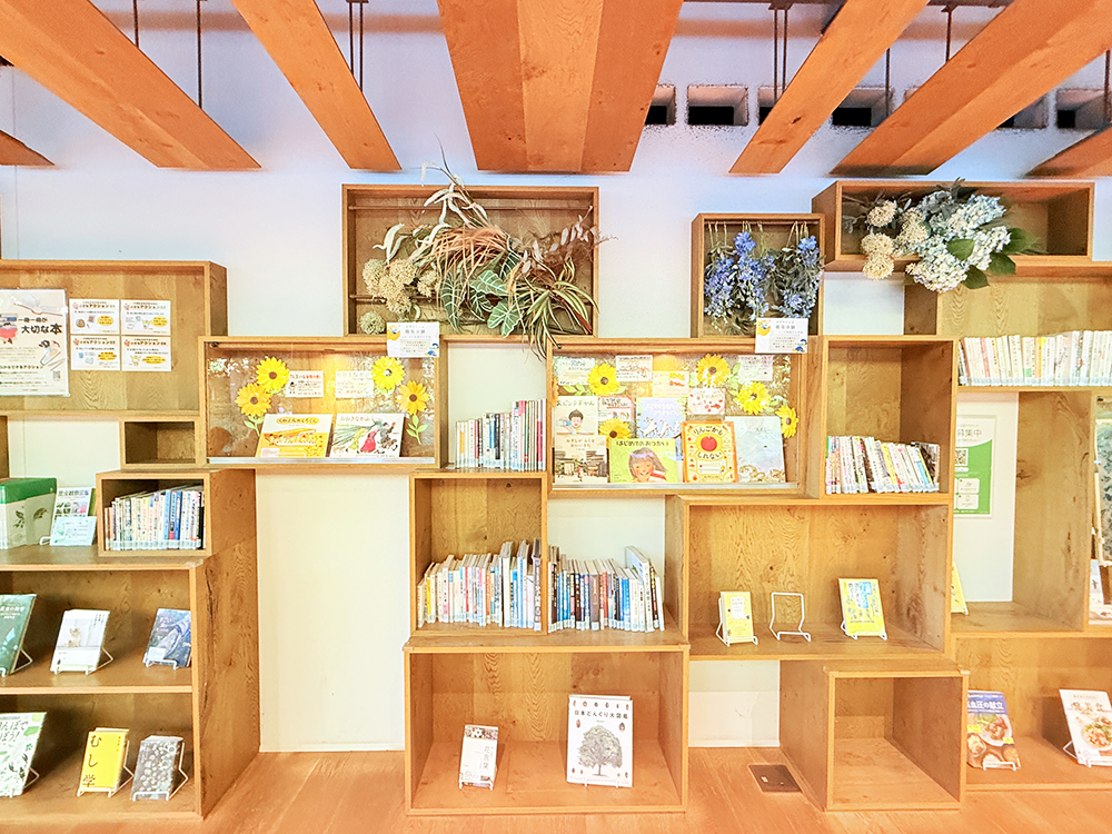 ひまわりの花などで夏らしく装飾された、せせらぎ館内の図書コーナー、せせらぎ文庫の木製の本棚
