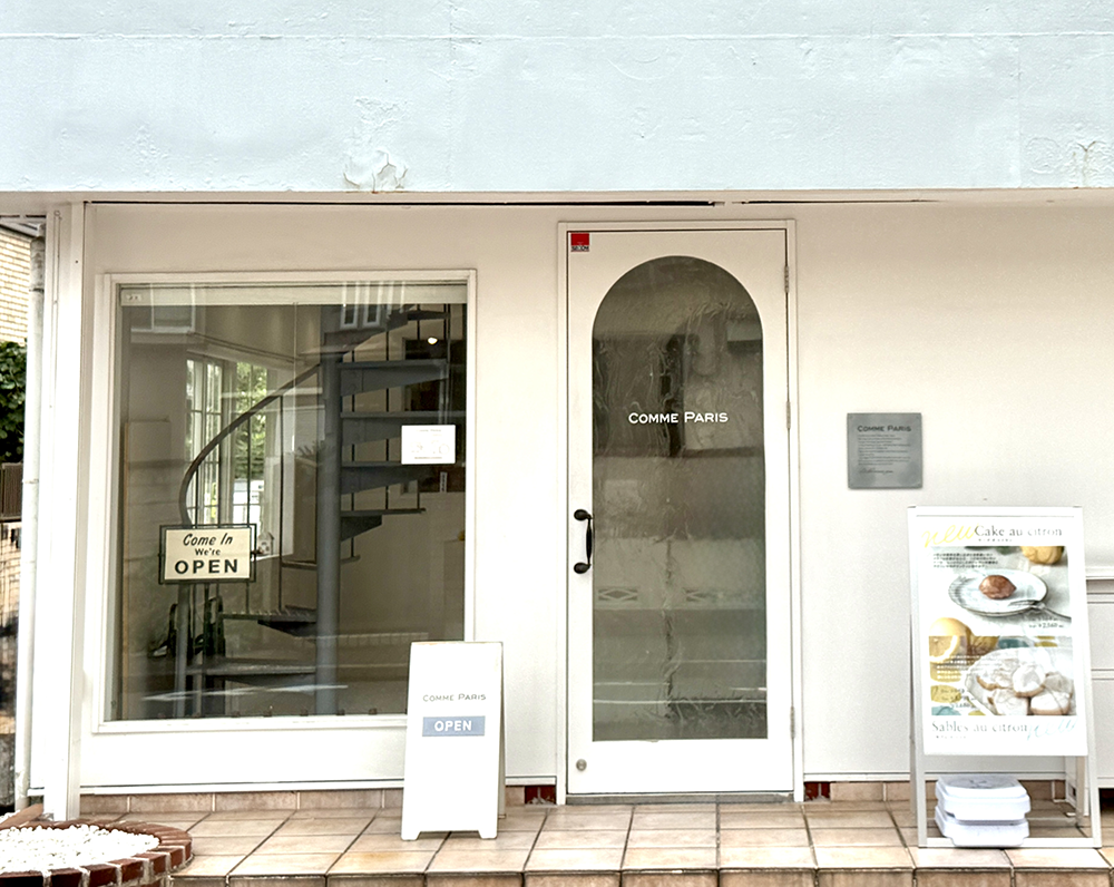 田園調布の住宅街に佇む、白を基調としたお洒落な外壁と、アーチ状のガラス扉が目を引く「COMME PARIS(コムパリ)」の洗練された店舗外観