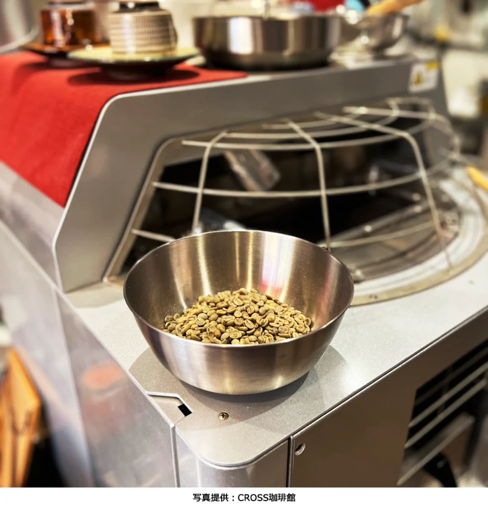 ボウルに入ったコーヒーの生豆とクロス珈琲館に導入されている業務用の焙煎機