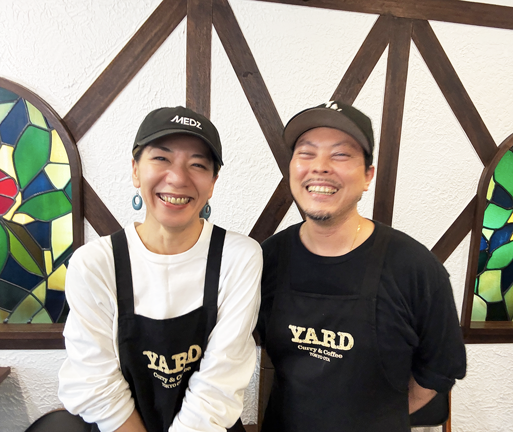お揃いのヤードロゴ入りエプロンとキャップを被り満面の笑みを見せるオーナーの小林さん夫妻